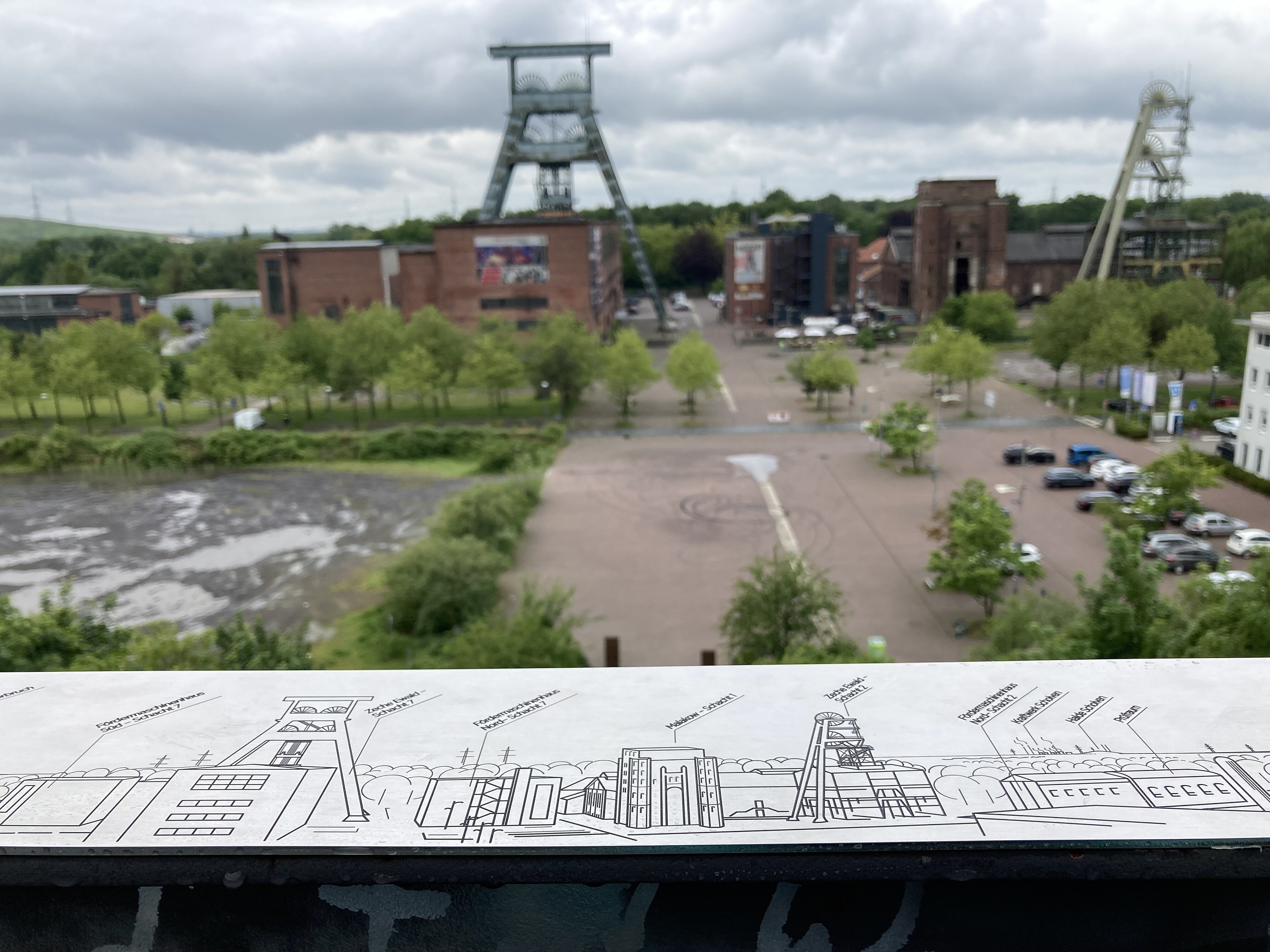 Panoramen_Halde Hoheward_Beschilderung_c_RVR Das Foto ist von einer Aussichtplattform mit Blicke auf die Zeche Ewald fotografiert. Im Vordergrund ist eine Metallplatte zu sehen, auf welche zeigt, was von der Aussichtsplattform zu sehen ist.